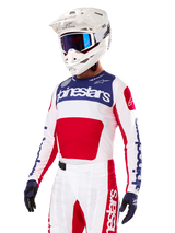 Pilota di motocross con maglia Alpinestars Limited Edition Techstar Fortitude, rosso acceso, bianco e blu, con casco bianco, occhiali blu e pantaloni coordinati, abbigliamento da gara ad alte prestazioni per competizioni off-road