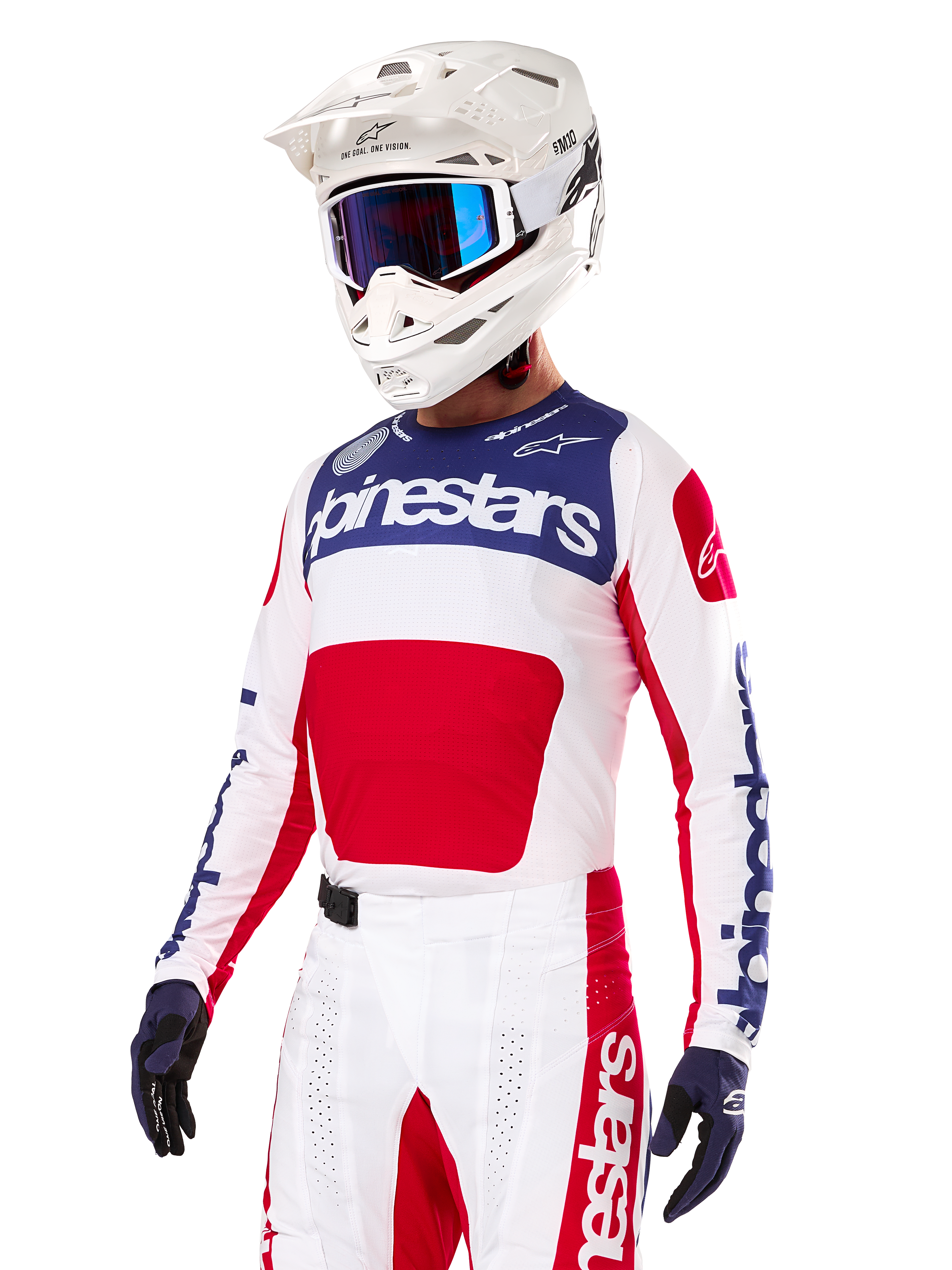 Pilota di motocross con maglia Alpinestars Limited Edition Techstar Fortitude, rosso acceso, bianco e blu, con casco bianco, occhiali blu e pantaloni coordinati, abbigliamento da gara ad alte prestazioni per competizioni off-road