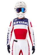 Alpinestars Maglia Limited Edition Techstar Fortitude, maglia da motocross bianca, rossa e blu, indossata con pantaloni e casco coordinati, con marchio Alpinestars e motto One Goal One Vision, dettagli traforati, design aerodinamico per prestazioni fuoristrada