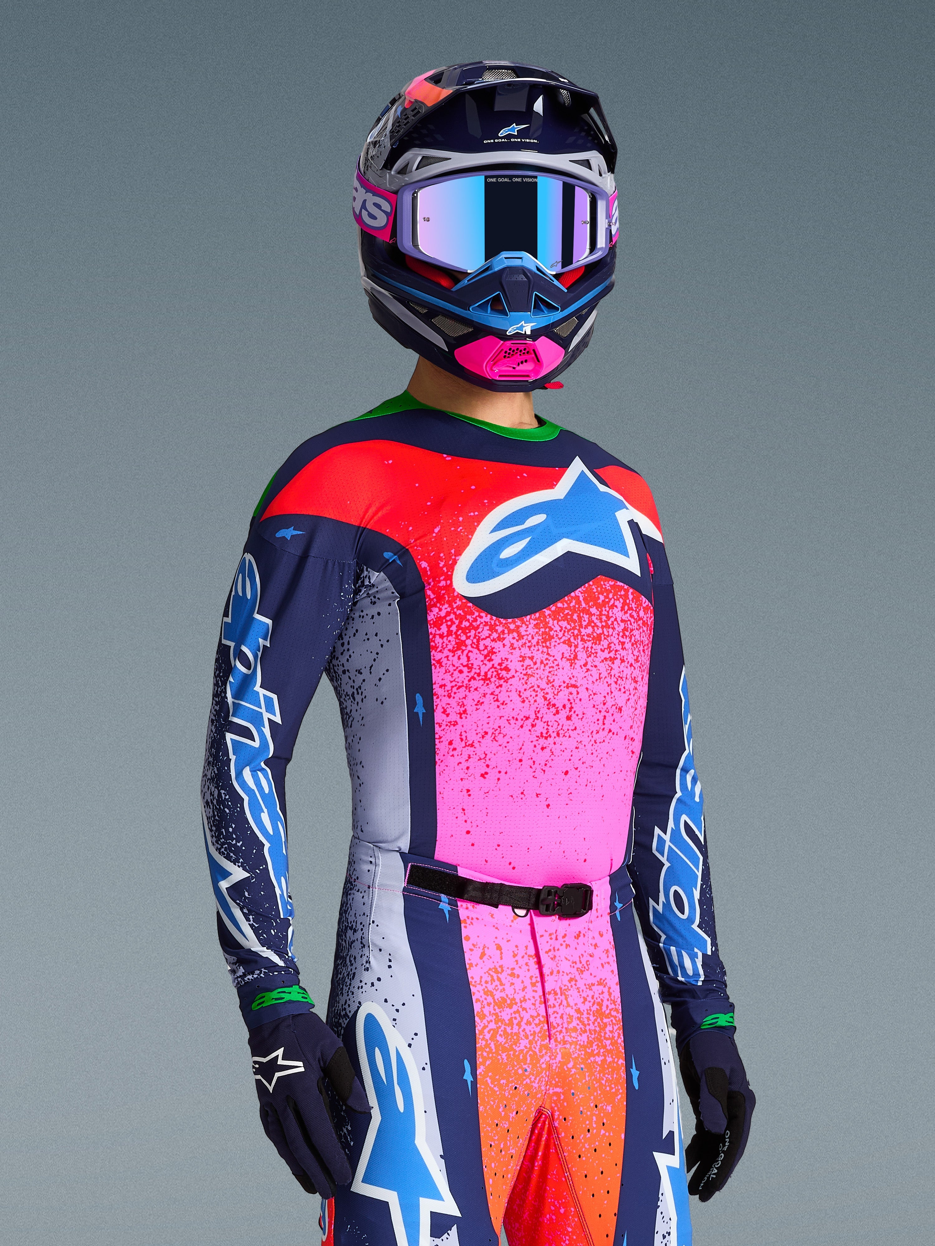 Alpinestars Limited Edition Supertech Records Jersey, maglia da motocross e completo coordinato, multicolore con accenti blu navy, rosa e arancione a effetto spruzzato, grande logo blu e bianco sul petto, indossata con casco e guanti coordinati, vestibilità atletica race-ready