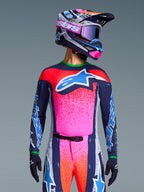 Pilota di motocross che indossa la maglia Alpinestars Limited Edition Supertech Records, design rosa vivace e blu navy con motivi punteggiati arancioni e logo a stella azzurro, casco e maschera coordinati, abbigliamento da gara professionale.