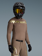 Alpinestars Maglia Supertech Air Gold edizione limitata, maglia da motocross da uomo, marrone e oro, vestibilità atletica con fori laser, indossata con casco e guanti.
