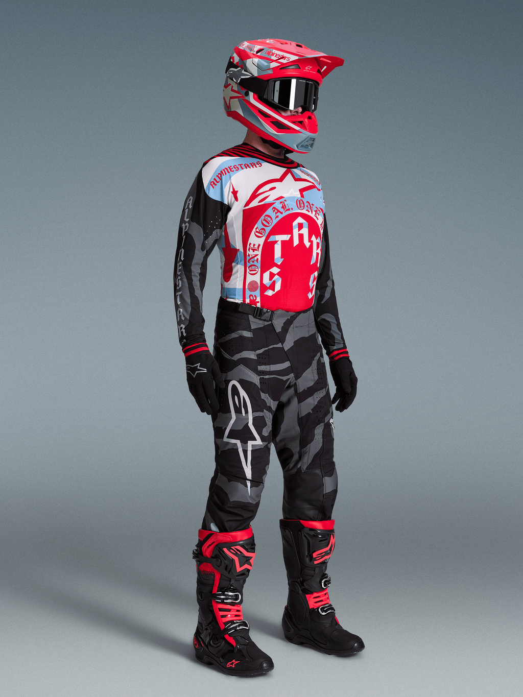 Set Alpinestars Techstar Beast Coast: maglia grafica, pantaloni mimetici grigi, casco rosso e stivali neri e rossi.