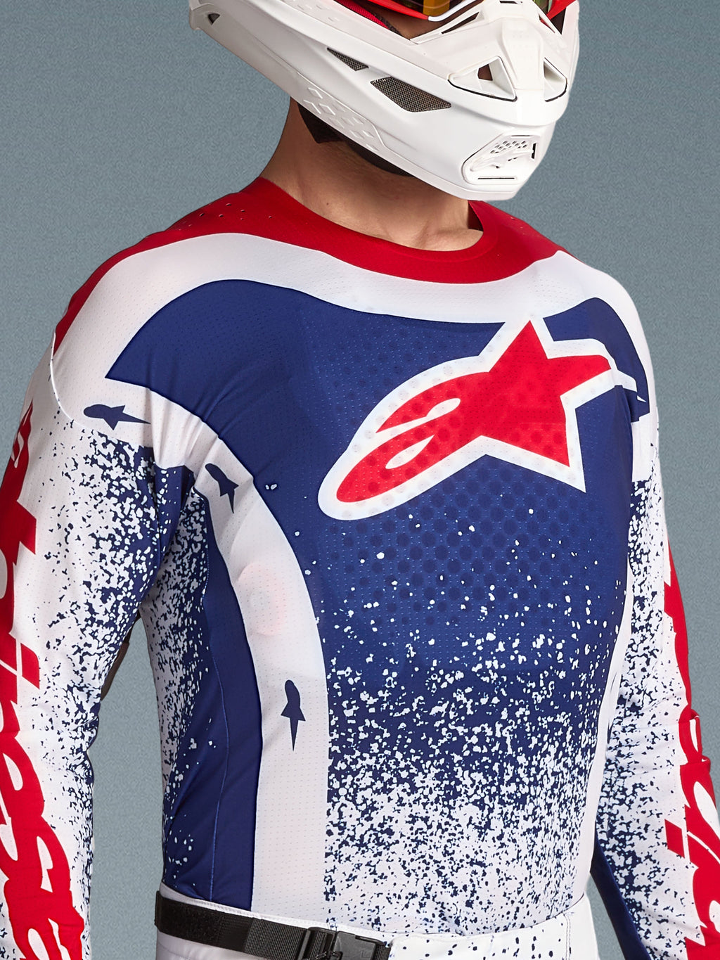 Alpinestars Techstar Unity Jersey Edizione Limitata, maglia da motocross da uomo, blu, bianca e rossa, logo a stella sul petto, indossata da un pilota con casco bianco per off-road
