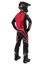 Pilota di motocross visto da dietro che indossa la maglia Supertech Ward 2024 in Black Red Berry, con pannello posteriore rosso e maniche nere con marchio Alpinestars bianco, abbinata a pantaloni coordinati, stivali Tech 10 neri e casco in fibra di carbonio nero.