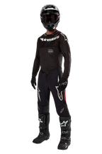 Pilota di motocross con equipaggiamento da gara completo, maglia Alpinestars Supertech Ward 2024 in Nero Rosso Berry, maglia nera con marchio Alpinestars bianco, pantaloni neri con pannelli laterali rossi e grandi loghi Astars bianchi, casco, guanti e stivali neri, completo coordinato di livello professionale per competizioni off-road