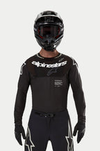 Pilota di motocross con maglia Alpinestars Supertech Ward 2024 in nero, vestibilità atletica da gara, logo Alpinestars bianco sul petto, perforazioni tagliate al laser e scritta 'Supertech Race Spec', abbinata a casco e occhiali neri per il fuoristrada.