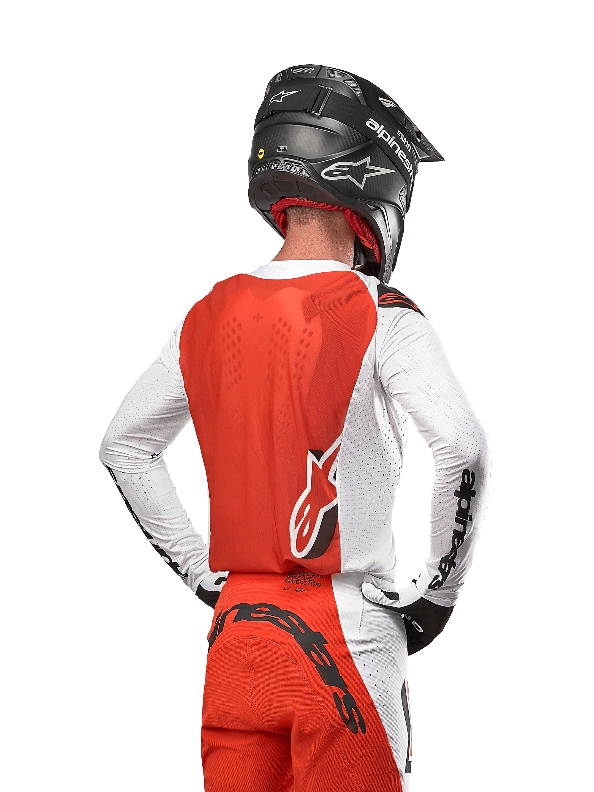 Pilota di motocross con maglia Alpinestars Supertech Ward 2024 in White Hot Orange, vista posteriore con pannello posteriore arancione e maniche bianche con branding Alpinestars nero, abbinata a pantaloni coordinati e casco nero, attrezzatura professionale per corse fuoristrada