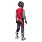 Alpinestars 2024 Supertech Dade Jersey, maglia da motocross, Iron Red Berry e grigio, vista posteriore su un pilota, con pannello posteriore rosso, logo grigio e maniche grigie, indossata con pantaloni da gara coordinati grigi e rossi, stivali bianchi e casco nero, abbigliamento professionale da fuoristrada.