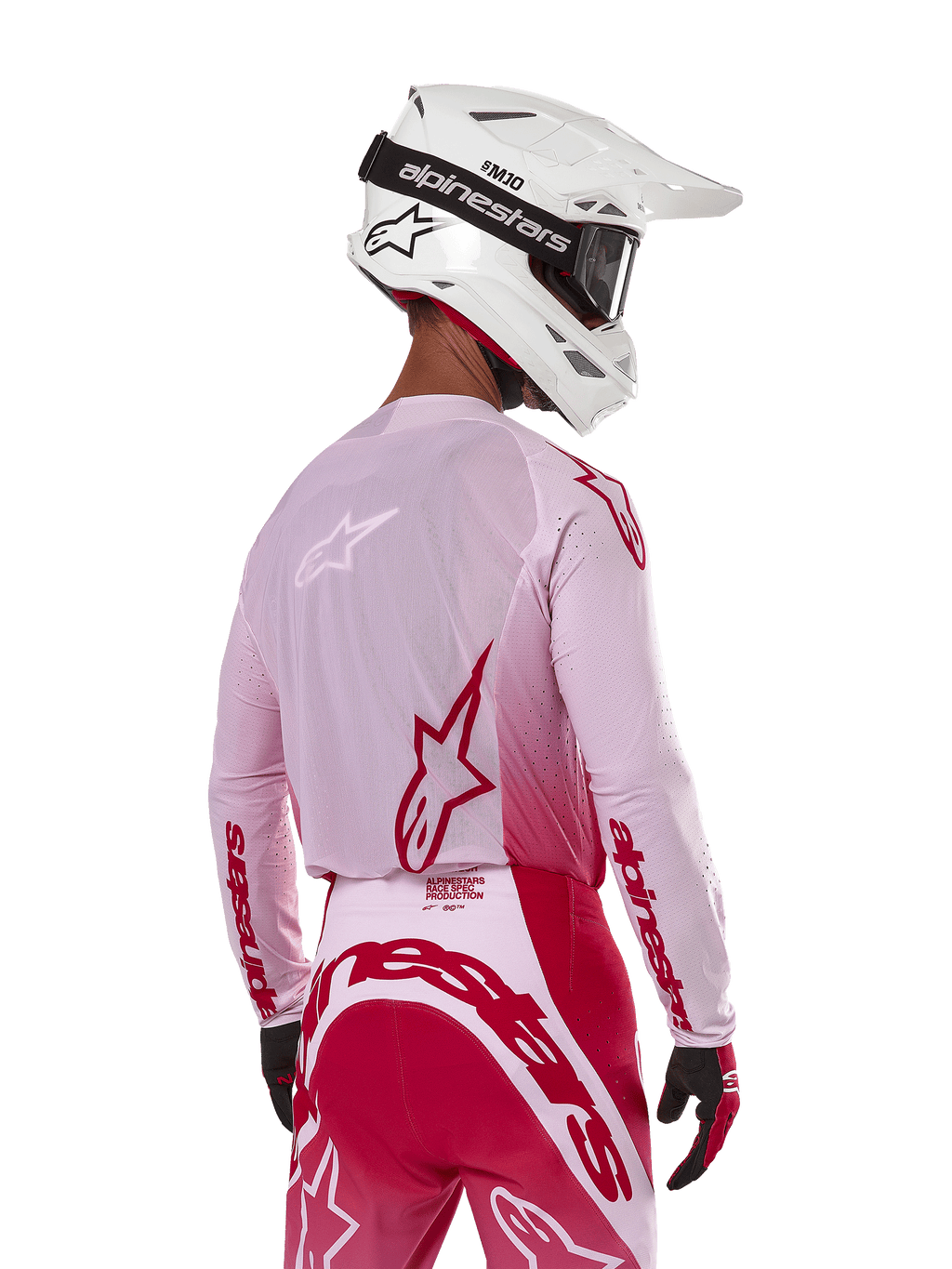 Pilota di motocross visto di spalle che indossa la maglia Alpinestars Supertech Dade 2024 in Red Berry Lilac, con pannelli in rete traspirante e loghi Alpinestars rossi, abbinata a pantaloni coordinati rossi e lilla e un casco Alpinestars bianco con maschera, abbigliamento professionale da gara off-road