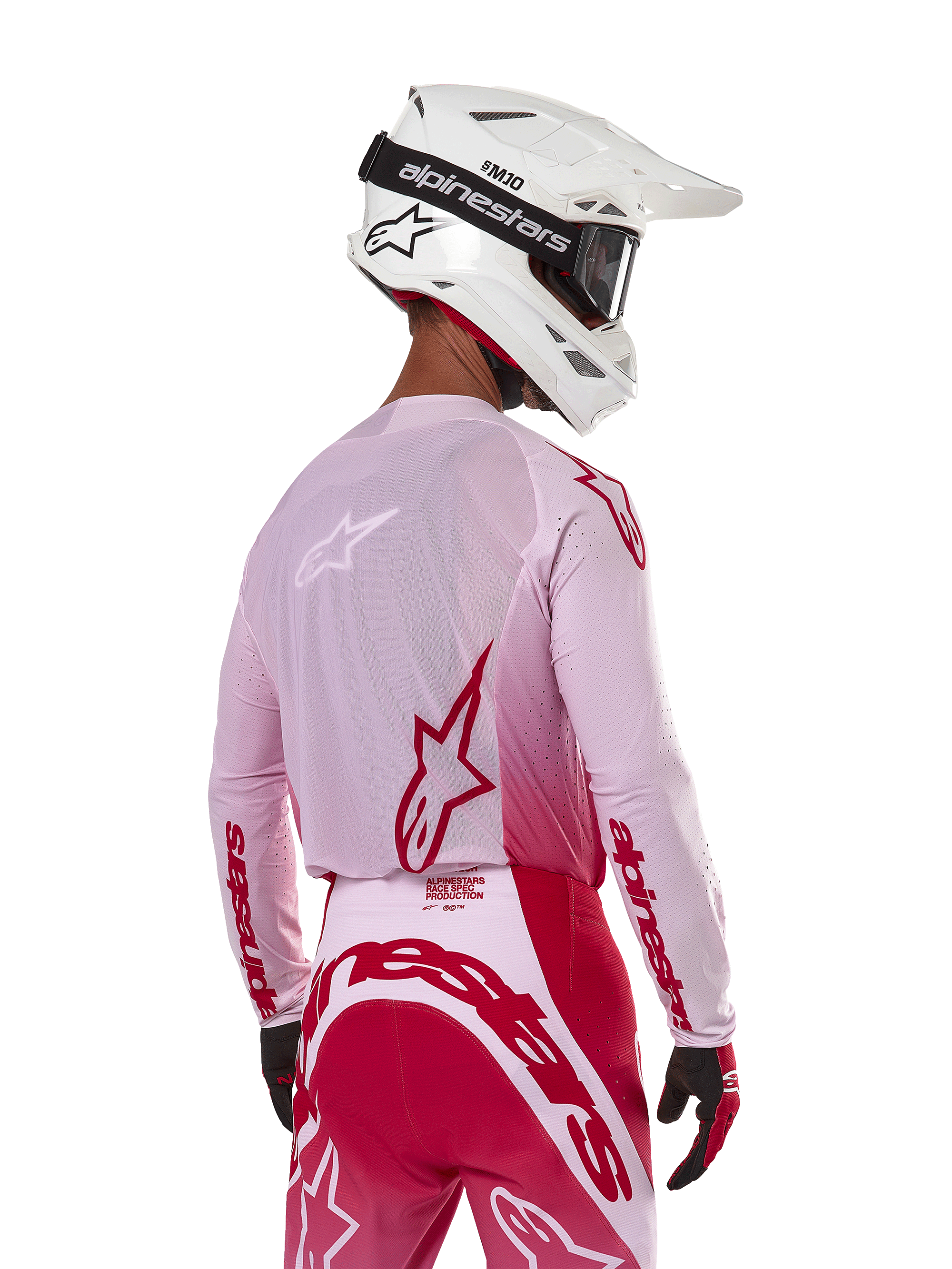 Pilota di motocross visto di spalle che indossa la maglia Alpinestars Supertech Dade 2024 in Red Berry Lilac, con pannelli in rete traspirante e loghi Alpinestars rossi, abbinata a pantaloni coordinati rossi e lilla e un casco Alpinestars bianco con maschera, abbigliamento professionale da gara off-road