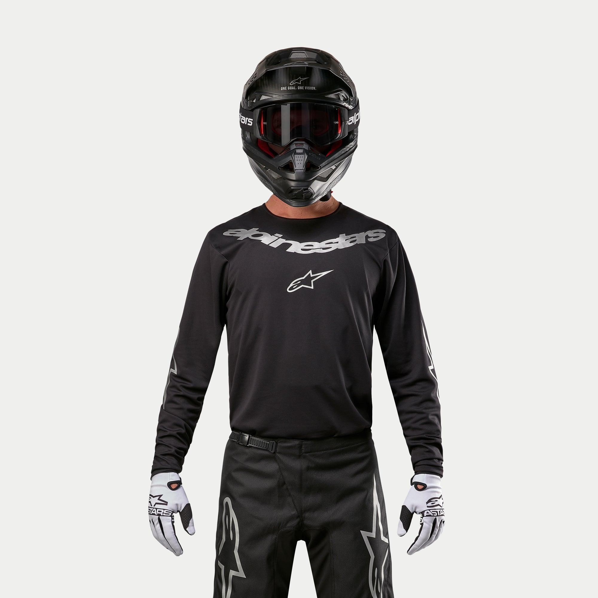 Maglia Alpinestars Fluid Graphite 2024, maglia da motocross nero e argento, indossata da un pilota con casco nero e occhiali rossi, con logo Alpinestars argento sul petto, coordinata con pantaloni neri e guanti bianchi per prestazioni fuoristrada