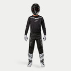 Pilota di motocross con equipaggiamento da gara completo, maglia Alpinestars 2024 Fluid Graphite in nero argento, pantaloni neri con loghi a stella argentati, casco nero con occhiali rossi, stivali bianchi e neri, guanti bianchi e neri, completo da motocross coordinato