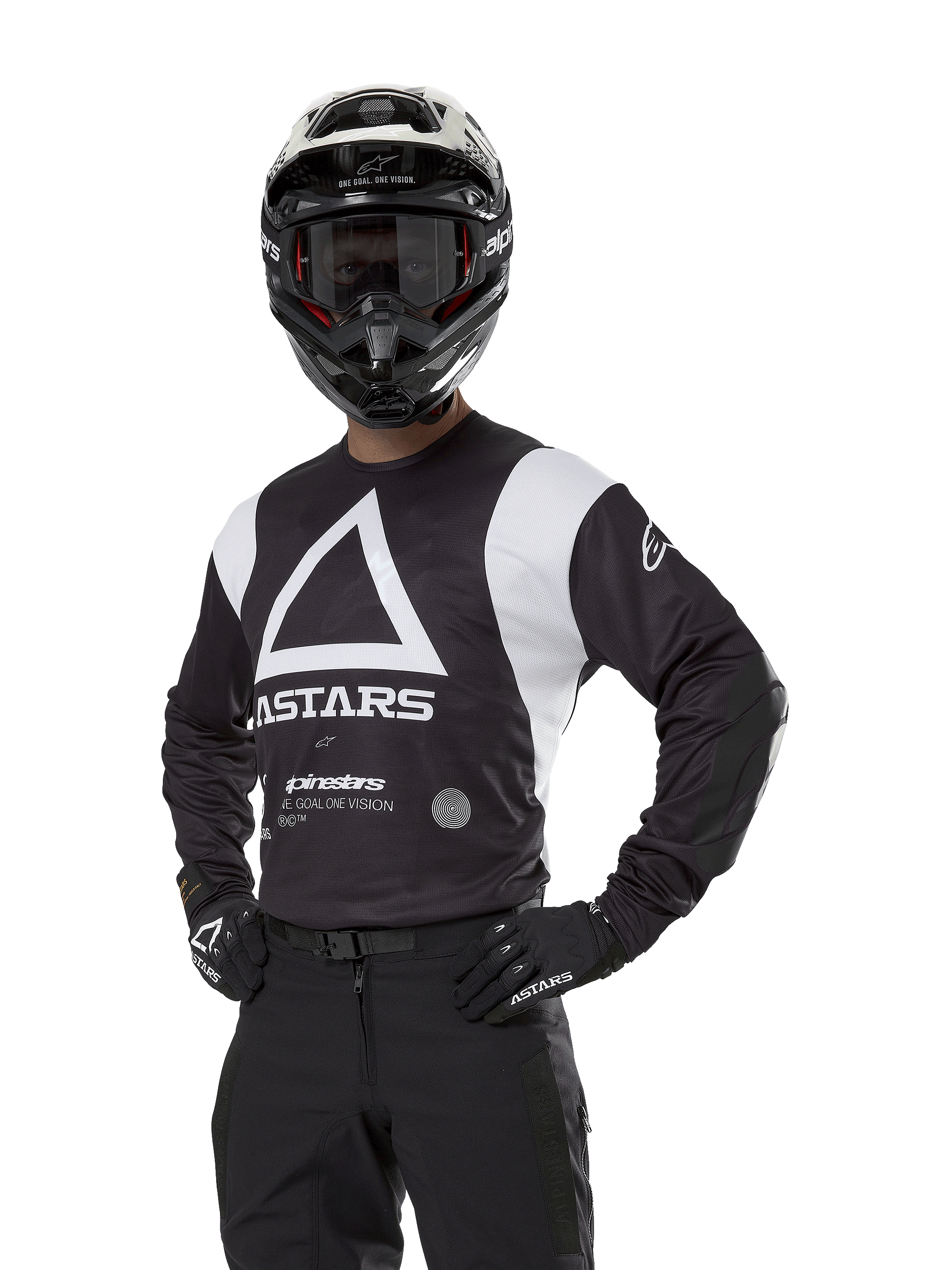 Alpinestars Techdura Jersey, maglia da motocross, nera e bianca, indossata con casco e guanti abbinati, posa con mani sui fianchi su sfondo bianco, con grande logo a triangolo 'A' e marchio ASTARS