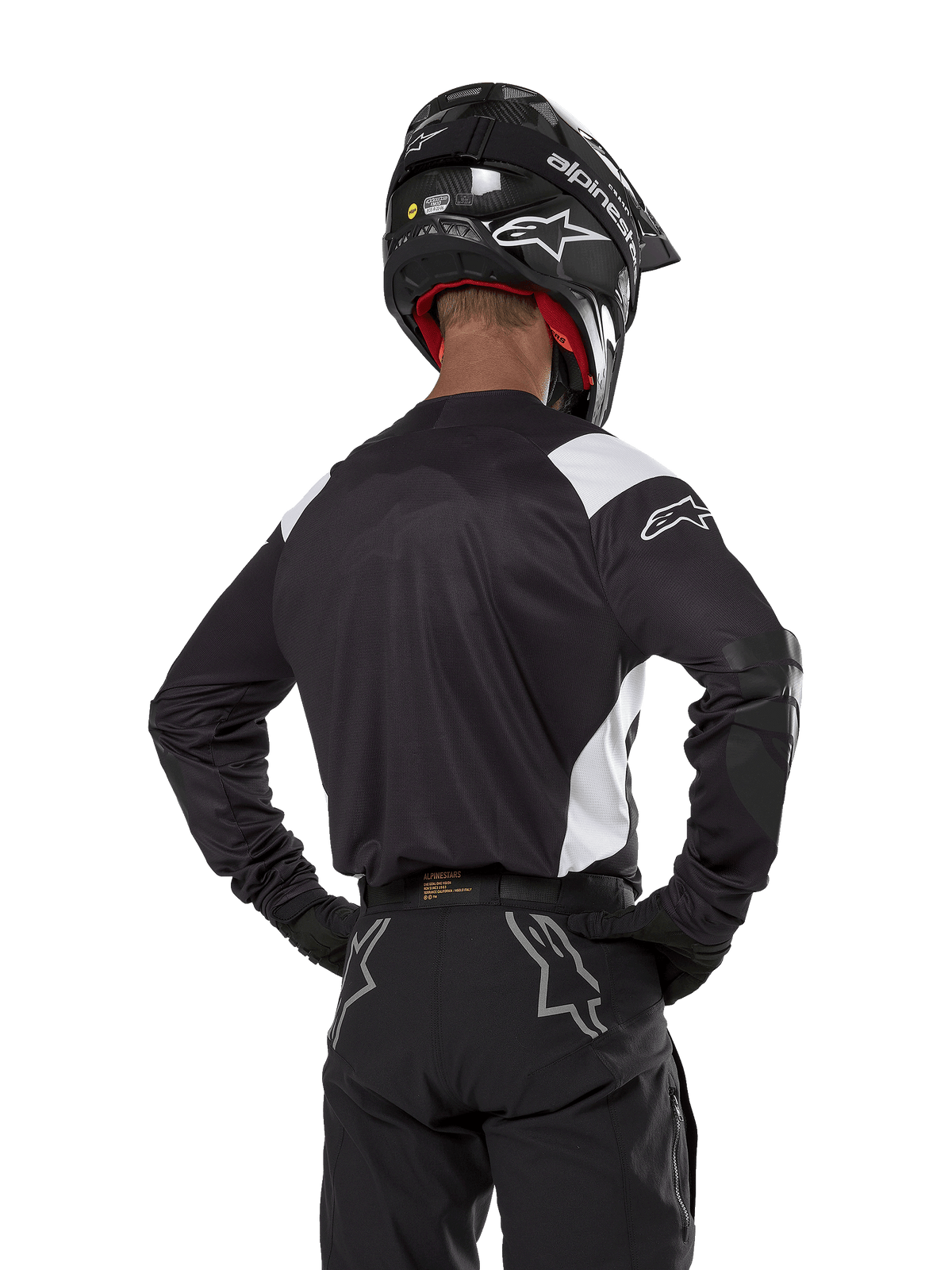 Alpinestars Techdura Jersey, nera con accenti bianchi sulle spalle, vista posteriore di un pilota di motocross con pantaloni e casco neri coordinati, toppe rinforzate sui gomiti, abbigliamento per enduro e gare fuoristrada