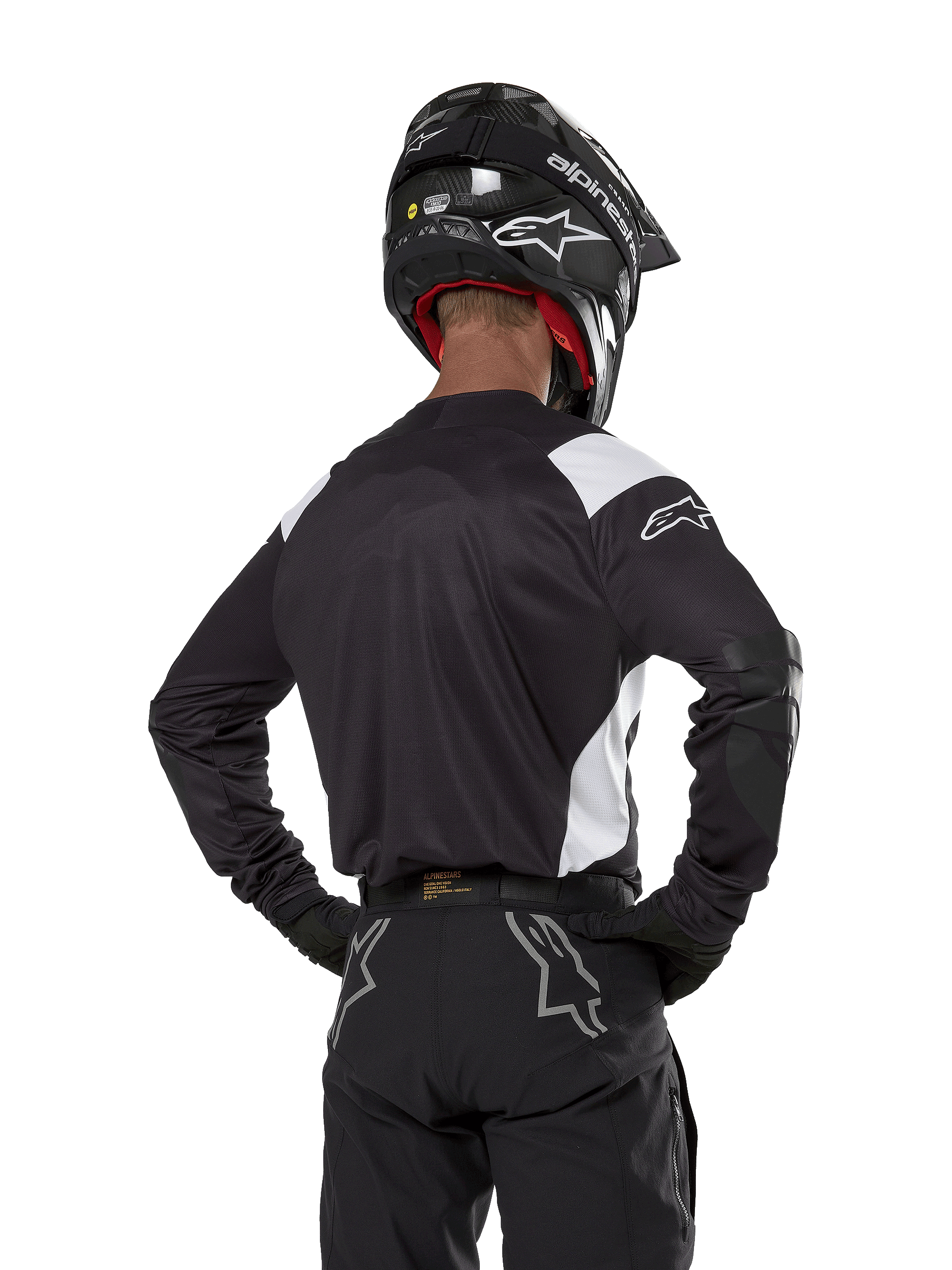 Alpinestars Techdura Jersey, nera con accenti bianchi sulle spalle, vista posteriore di un pilota di motocross con pantaloni e casco neri coordinati, toppe rinforzate sui gomiti, abbigliamento per enduro e gare fuoristrada
