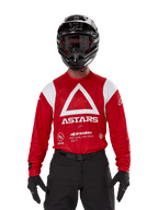 Pilota di motocross con maglia Alpinestars Techdura, Rosso Brillante con grafiche bianche, caratterizzata da un grande triangolo bianco e logo ASTARS sul petto, abbinata a casco nero, occhiali neri e attrezzatura da guida nera, completo coordinato per enduro e corse fuoristrada