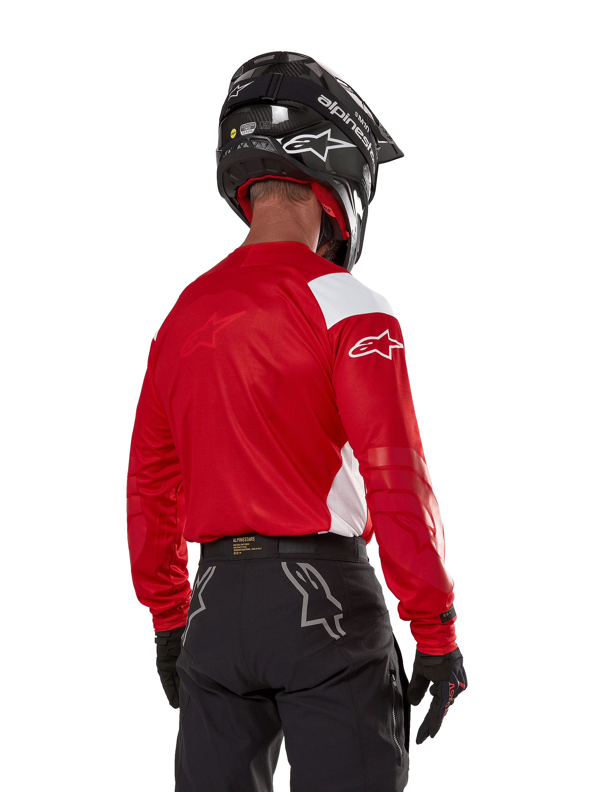 Pilota di motocross visto dal retro che indossa la maglia Alpinestars Techdura in rosso vivo con pannelli bianchi, abbinata a pantaloni da fuoristrada neri, casco nero e guanti neri, abbigliamento coordinato per la guida enduro e motocross.