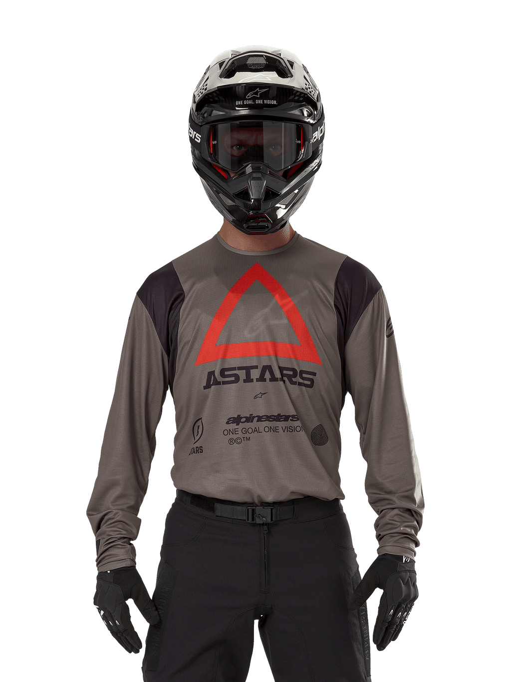 Pilota di motocross con maglia Alpinestars Techdura in Falcon Brown, caratterizzata da un evidente triangolo rosso e logo 'ASTARS' sul petto, abbinata a pantaloni neri, casco nero con occhiali e guanti neri, abbigliamento completo da enduro