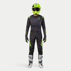 Pilota di motocross con equipaggiamento completo da gara, maglia Techstar Rantera 2024 in nero, navy e giallo fluo, pantaloni coordinati con stampa astratta, casco giallo fluo brillante, stivali bianchi e neri, outfit coordinato per corse off-road