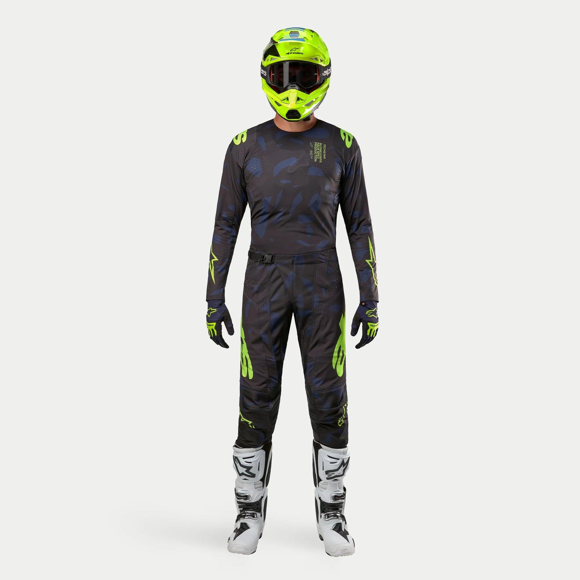 Pilota di motocross con equipaggiamento completo da gara, maglia Techstar Rantera 2024 in nero, navy e giallo fluo, pantaloni coordinati con stampa astratta, casco giallo fluo brillante, stivali bianchi e neri, outfit coordinato per corse off-road