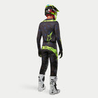 Maglia Alpinestars Techstar Rantera 2024, maglia da motocross, nero, navy e giallo fluo, indossata con pantaloni coordinati, stivali bianchi e neri e casco giallo fluo, vista dal retro in abbigliamento completo da fuoristrada