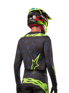 Vista posteriore di un pilota di motocross con maglia Alpinestars 2024 Techstar Rantera in Black Navy Yellow Fluo, caratterizzata da loghi giallo fluo prominenti sulla schiena, abbinata a pantaloni coordinati e casco giallo neon per un look completo da off-road.