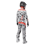 Pilota di motocross visto da dietro con maglia Alpinestars 2024 Techstar Rantera e pantaloni coordinati, motivo Haze Gray Camo con vivaci loghi Alpinestars rossi, casco nero, stivali bianchi e neri, guanti neri, set completo di abbigliamento da motocross coordinato.