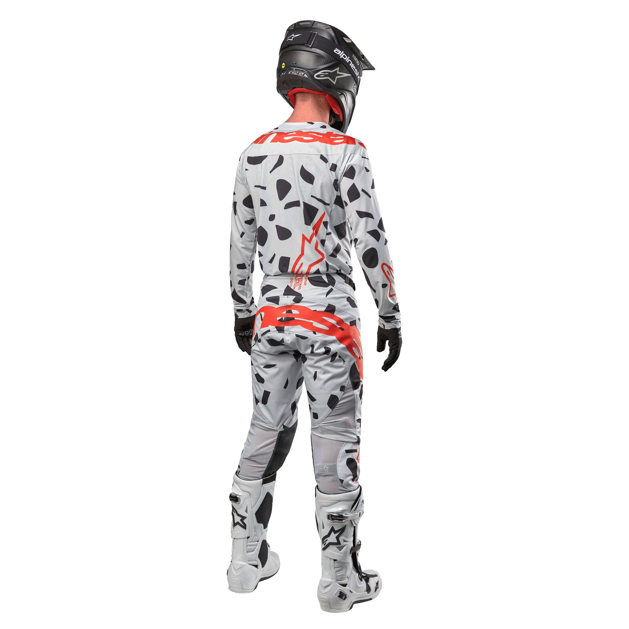 Pilota di motocross visto da dietro con maglia Alpinestars 2024 Techstar Rantera e pantaloni coordinati, motivo Haze Gray Camo con vivaci loghi Alpinestars rossi, casco nero, stivali bianchi e neri, guanti neri, set completo di abbigliamento da motocross coordinato.
