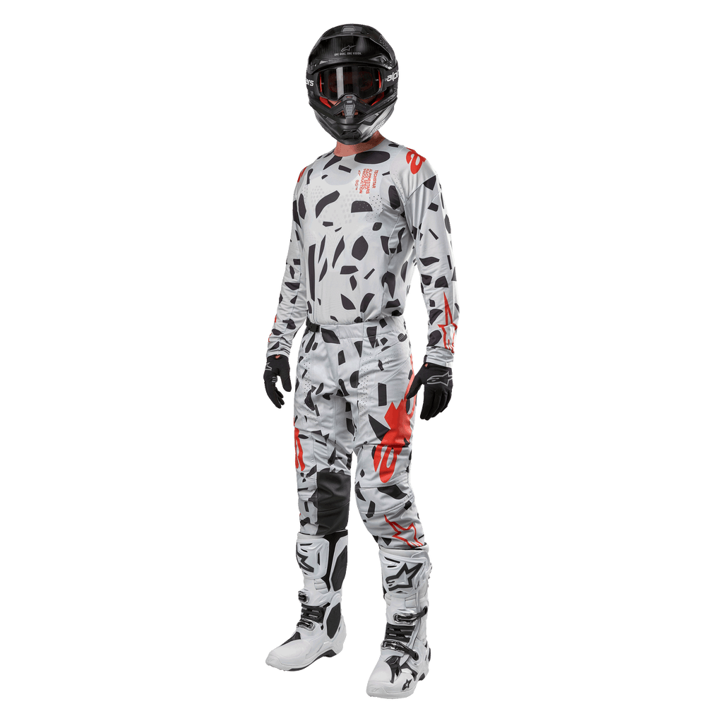 Pilota di motocross con maglia Alpinestars 2024 Techstar Rantera in Haze Gray Camo, pantaloni coordinati con accenti rossi e neri, casco e occhiali neri, guanti neri, stivali bianchi e neri, abbigliamento completo da motocross per prestazioni off-road