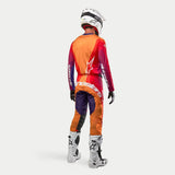 Completo da motocross Alpinestars Techstar Pneuma 2024, maglia e pantaloni viola scuro e arancione con loghi bianchi, indossato con casco e stivali bianchi, vista posteriore