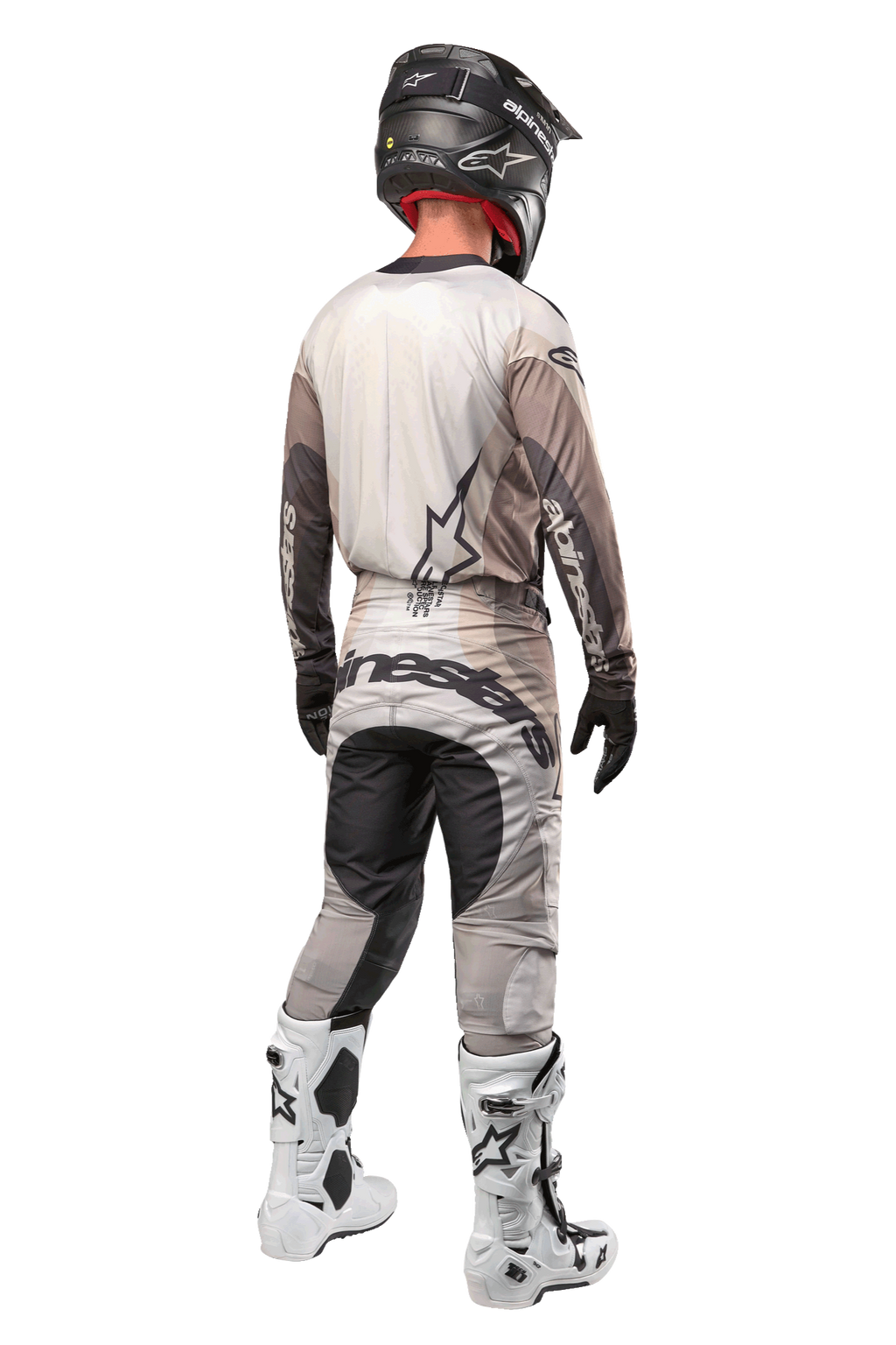 Pilota di motocross visto di spalle che indossa la maglia Techstar Pneuma 2024 in Dark Sand Iron Dust Gray, pantaloni da motocross coordinati con branding evidente, casco nero e stivali da gara bianchi, abbigliamento professionale coordinato da fuoristrada.