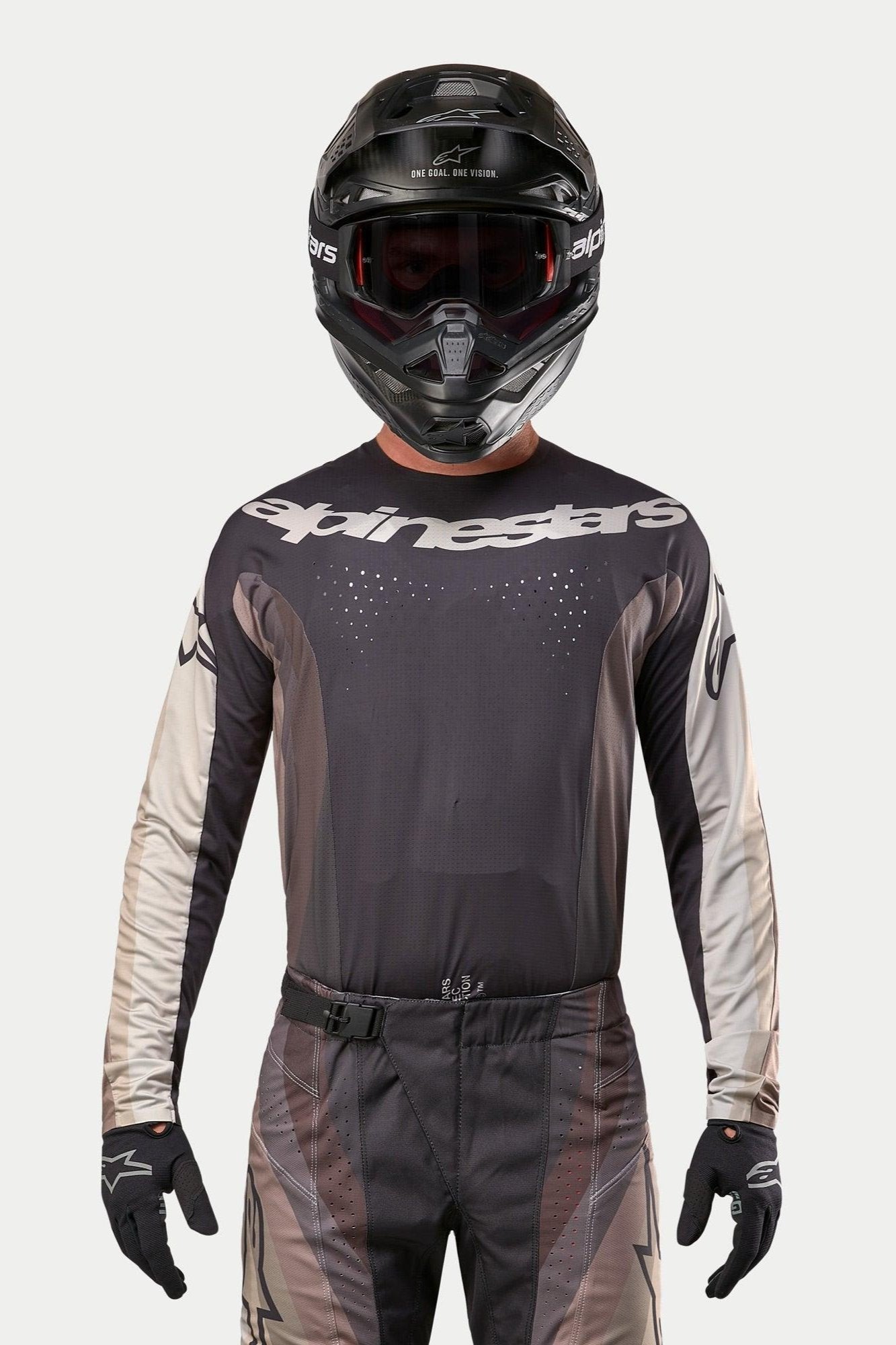 Alpinestars Techstar Pneuma Jersey 2024, maglia da motocross, Dark Sand e Iron Dust Gray, indossata con pantaloni da motocross coordinati e un casco nero, con logo Alpinestars sul petto e perforazioni per la ventilazione tagliate al laser, abbigliamento tecnico da gara off-road