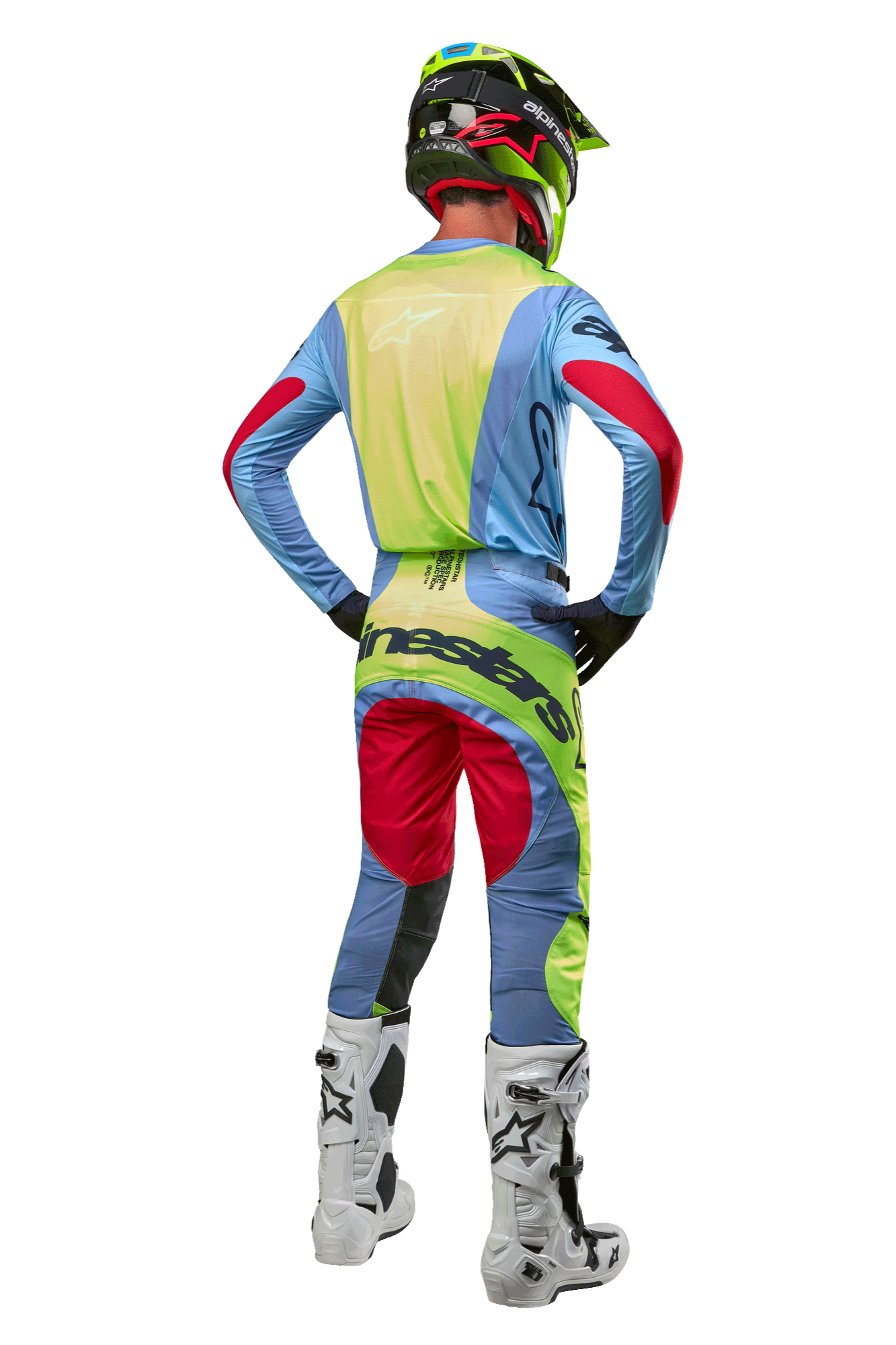 Pilota di motocross visto di spalle con maglia Alpinestars Techstar Ocuri 2024, celeste con accenti giallo fluo e rosso berry, pantaloni da gara coordinati, stivali bianchi e casco neon, equipaggiamento completo da fuoristrada per competizioni professionali