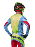 Pilota di motocross visto da dietro con maglia Alpinestars 2024 Techstar Ocuri, azzurro con retro giallo fluo e dettagli rossi sulle maniche, pantaloni da motocross coordinati e casco giallo neon, completo per gare fuoristrada