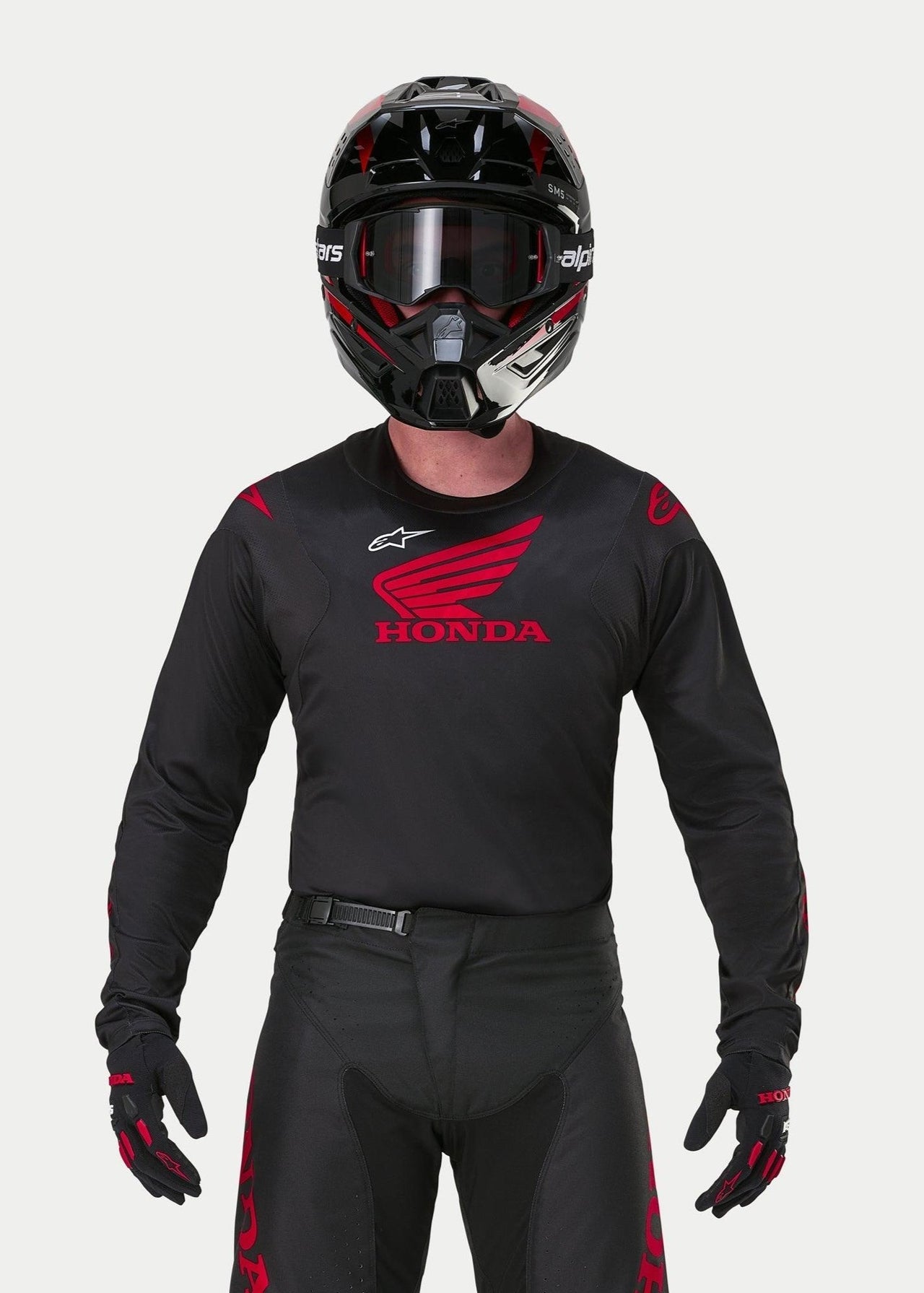 Pilota di motocross con maglia Alpinestars Honda Racer Iconic nero e rosso, grande logo Honda ad ala rosso sul petto e logo Astar bianco, abbinata a casco, occhiali e guanti neri per un kit completo da gara fuoristrada