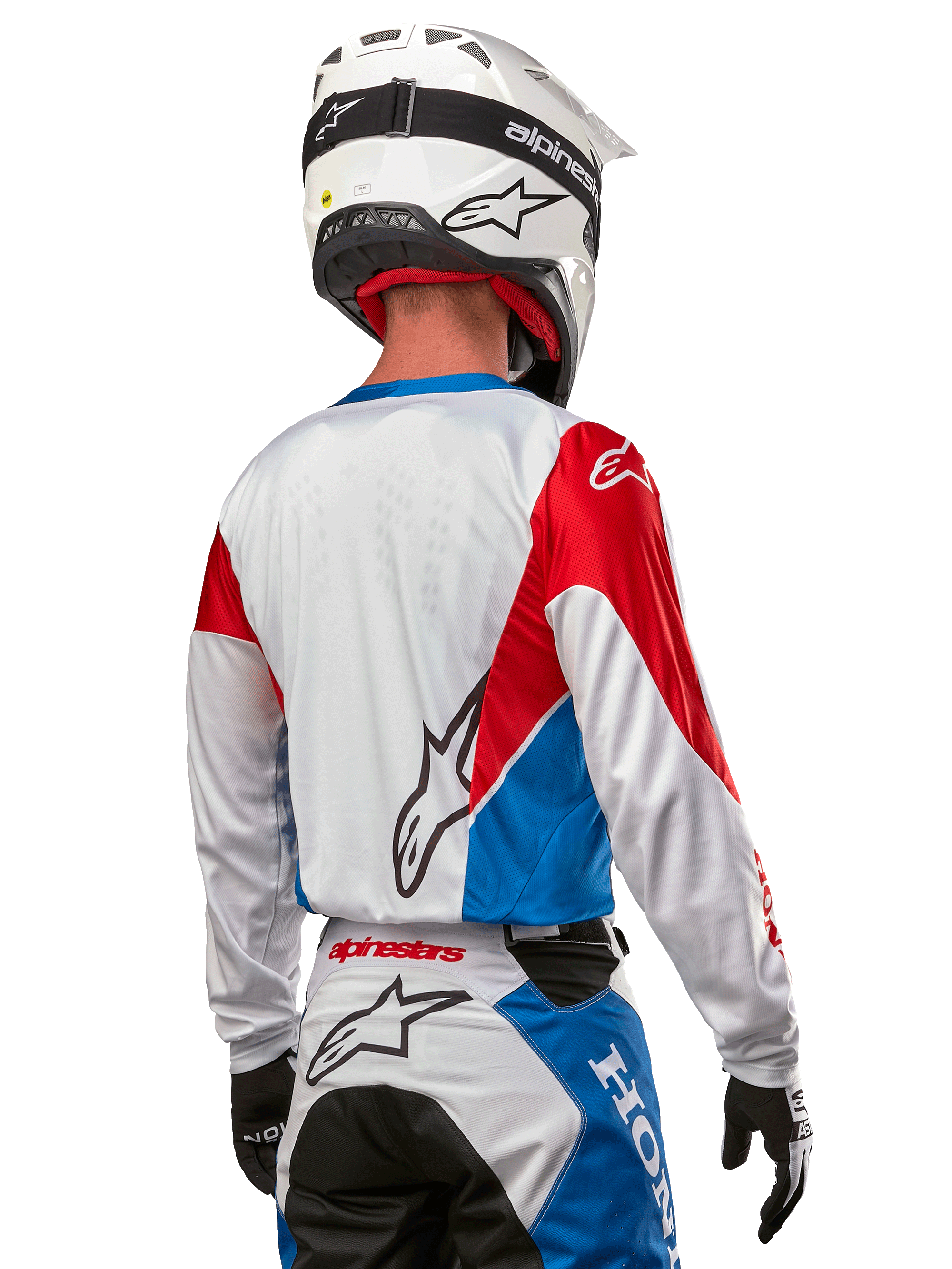 Pilota di motocross con maglia Alpinestars Honda Racer Iconic, vista posteriore, bianco con pannelli blu e rosso brillante, con logo Alpinestars sul retro, abbinata a casco bianco e pantaloni da motocross coordinati.