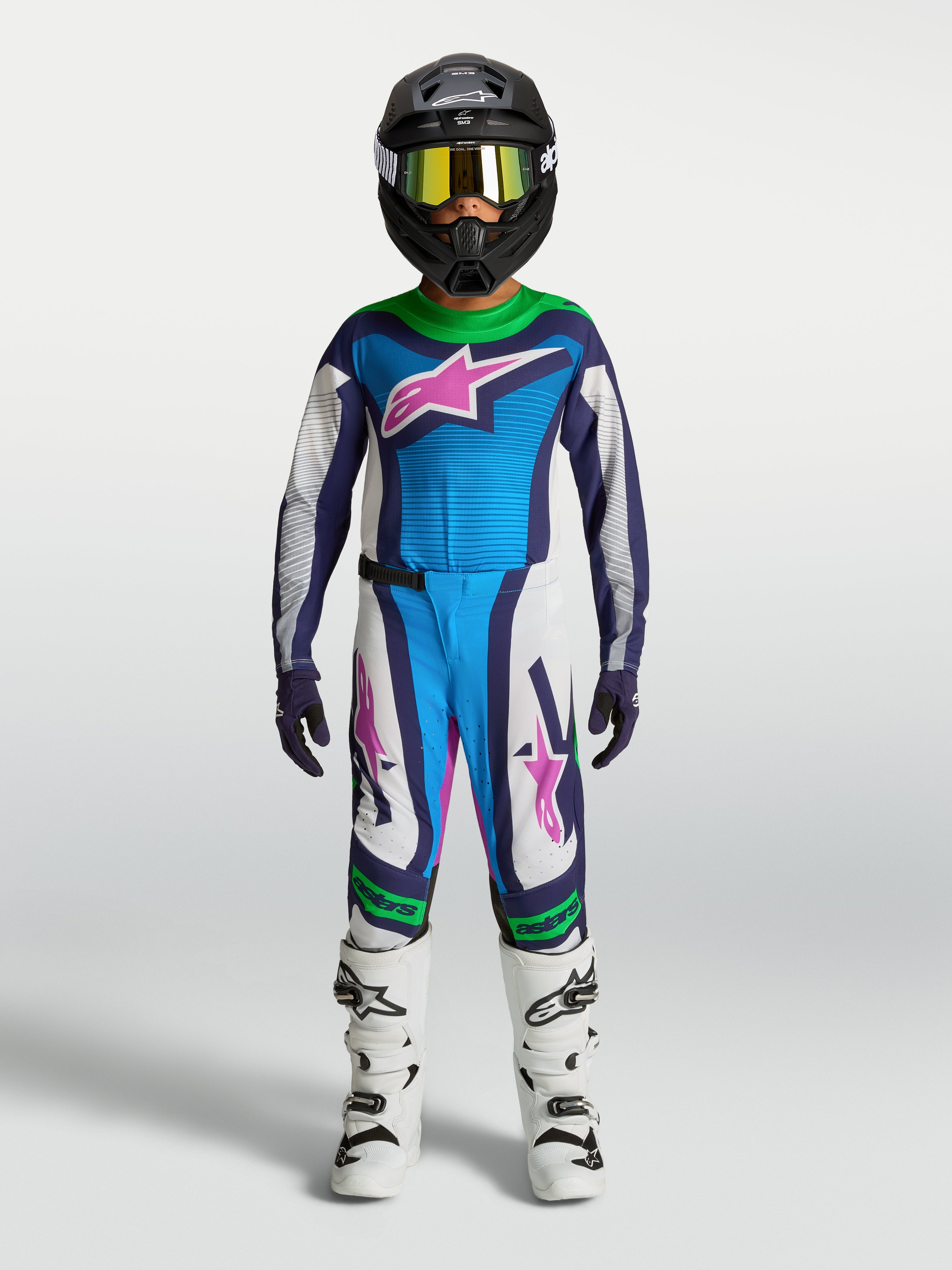 Alpinestars Ragazzo Supertech Maven Gear Set, completo da motocross blu e bianco con accenti verdi e rosa, su giovane pilota.