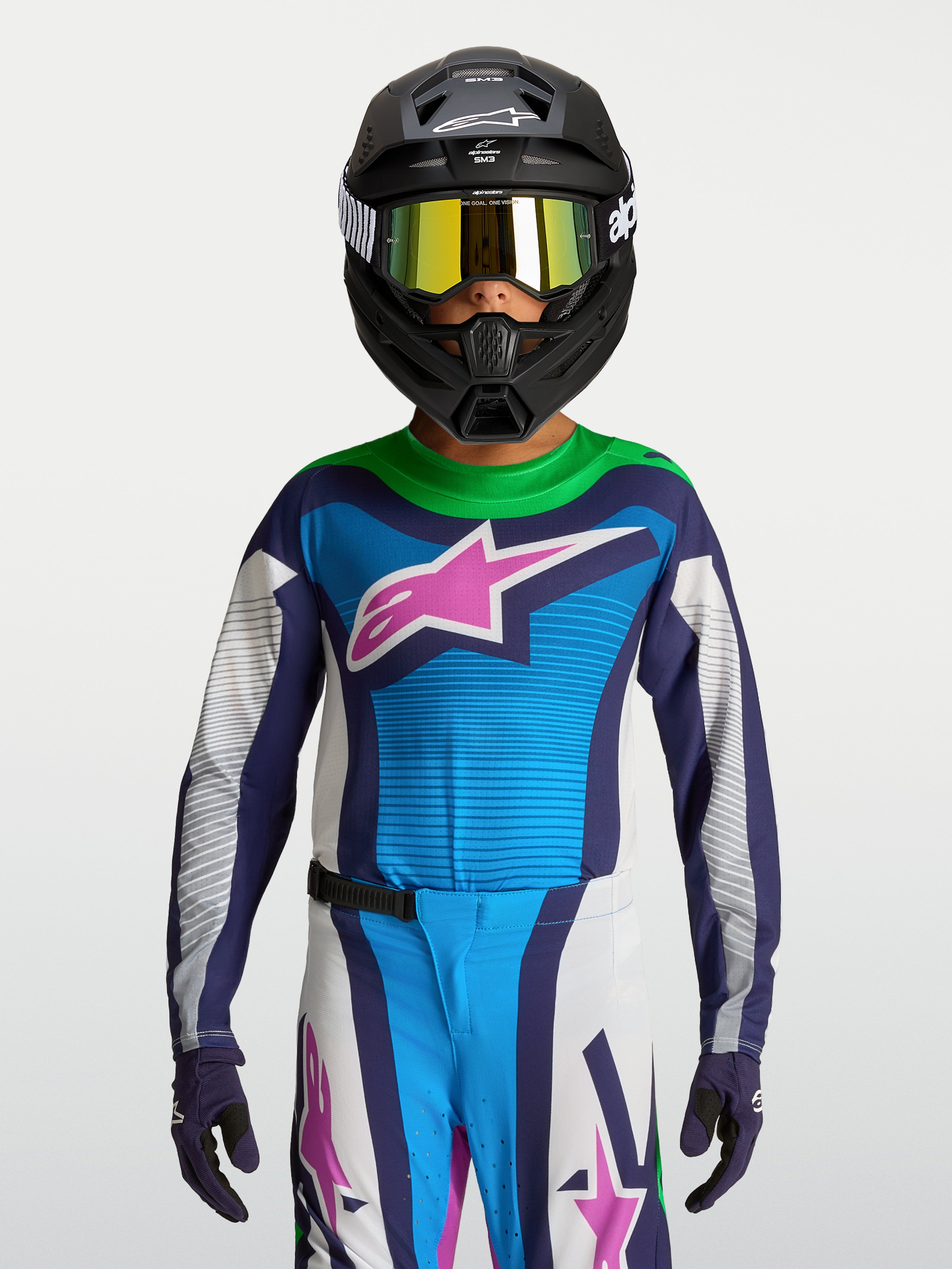 Alpinestars maglia Supertech Maven ragazzo 2027, maglia da motocross blu e bianca con accenti viola, indossata con casco e maschera per corse fuoristrada.