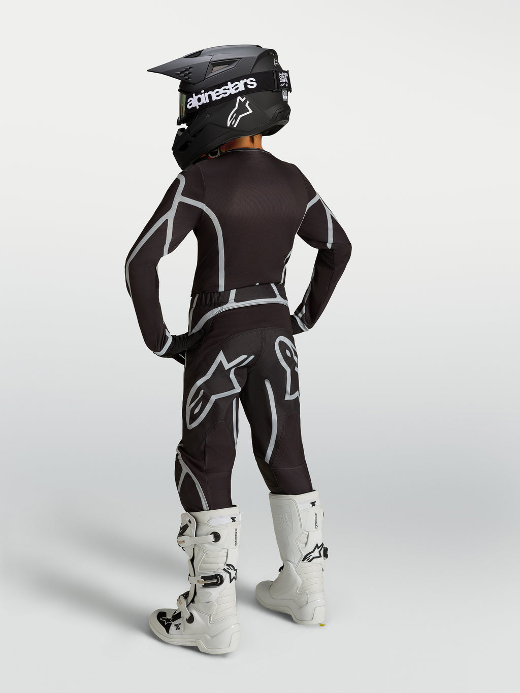 Alpinestars Ragazzo Fluid Apex V2 Gear Set 2027, completo da motocross nero e argento, vista posteriore con stivali bianchi