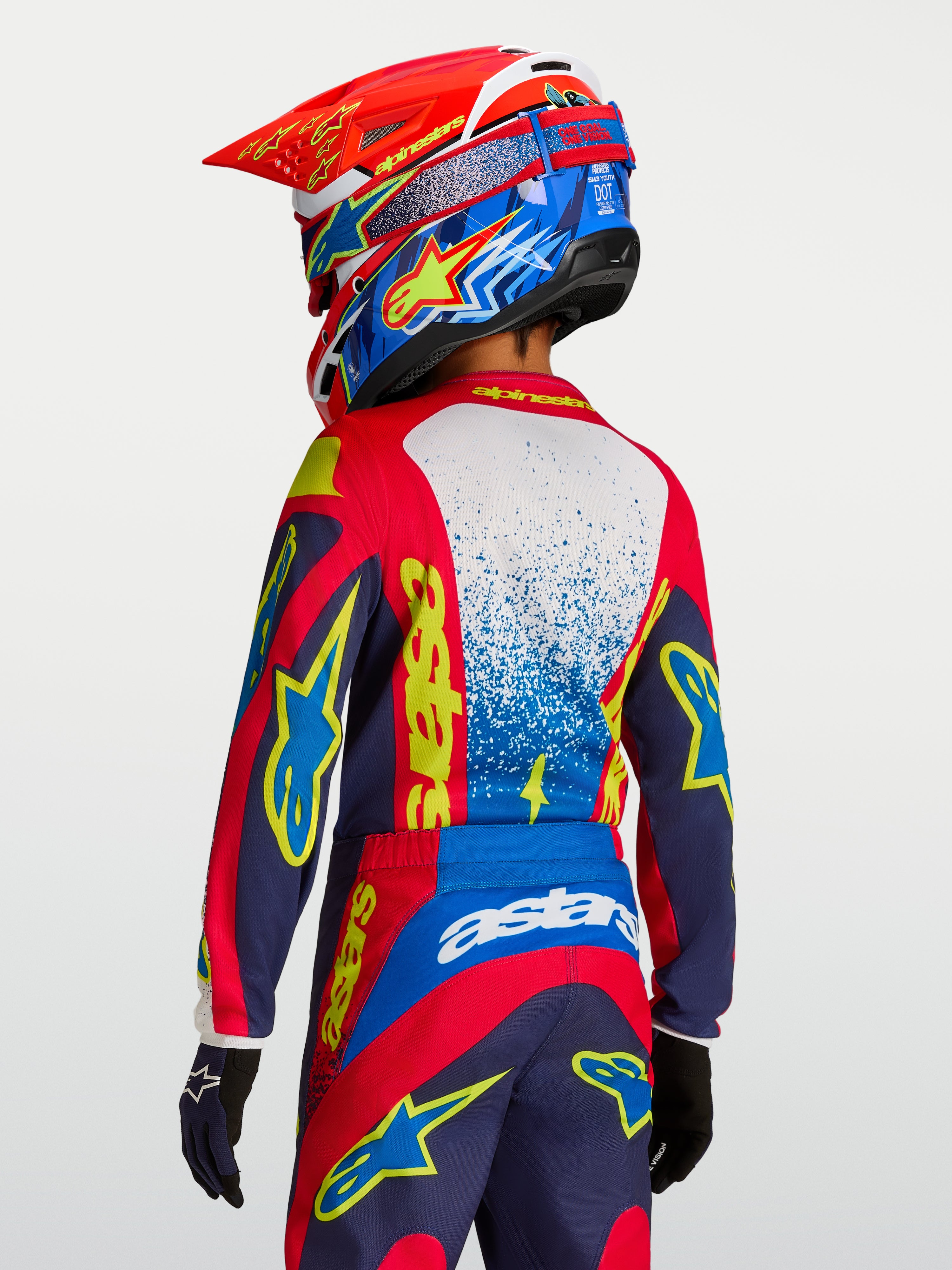 Alpinestars Maglia Fluid Drag Ragazzo 2027, maglia da motocross rossa, blu navy e gialla, vista posteriore su pilota.