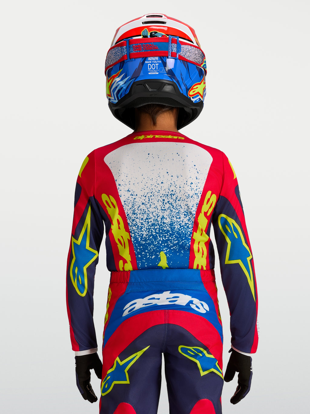 Alpinestars maglia Fluid Drag ragazzo 2027, maglia da motocross tecnica blu e rossa, vestibilità ergonomica per giovani piloti, vista posteriore con casco e guanti coordinati.