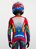 Alpinestars maglia Fluid Drag ragazzo 2027, maglia da motocross tecnica blu e rossa, vestibilità ergonomica per giovani piloti, vista posteriore con casco e guanti coordinati.