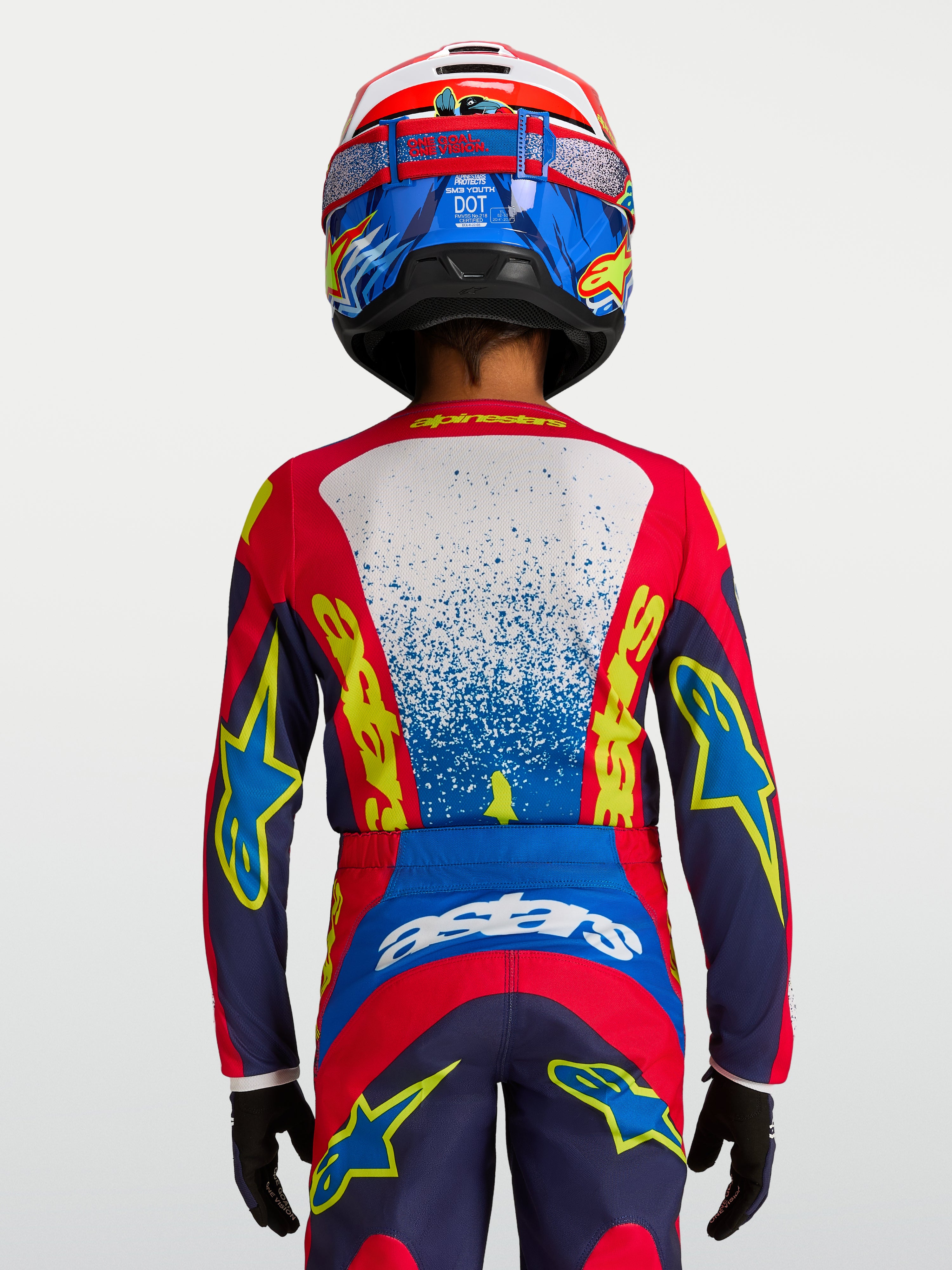 Alpinestars maglia Fluid Drag ragazzo 2027, maglia da motocross tecnica blu e rossa, vestibilità ergonomica per giovani piloti, vista posteriore con casco e guanti coordinati.
