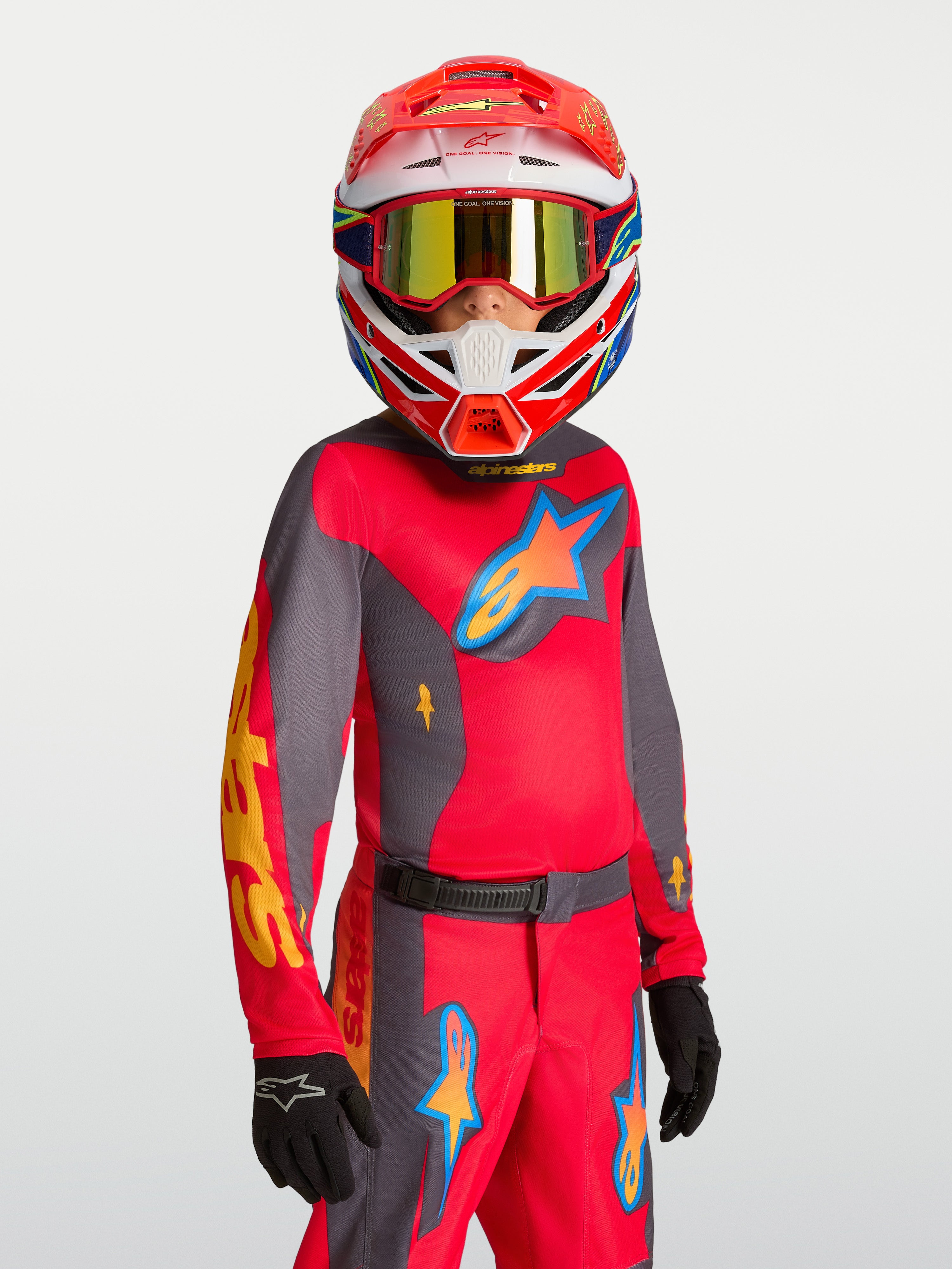 Alpinestars Maglia Fluid Hunt Ragazzo 2027, maglia da motocross rossa e grigia, traspirante per off-road, indossata da un giovane pilota con casco e guanti coordinati