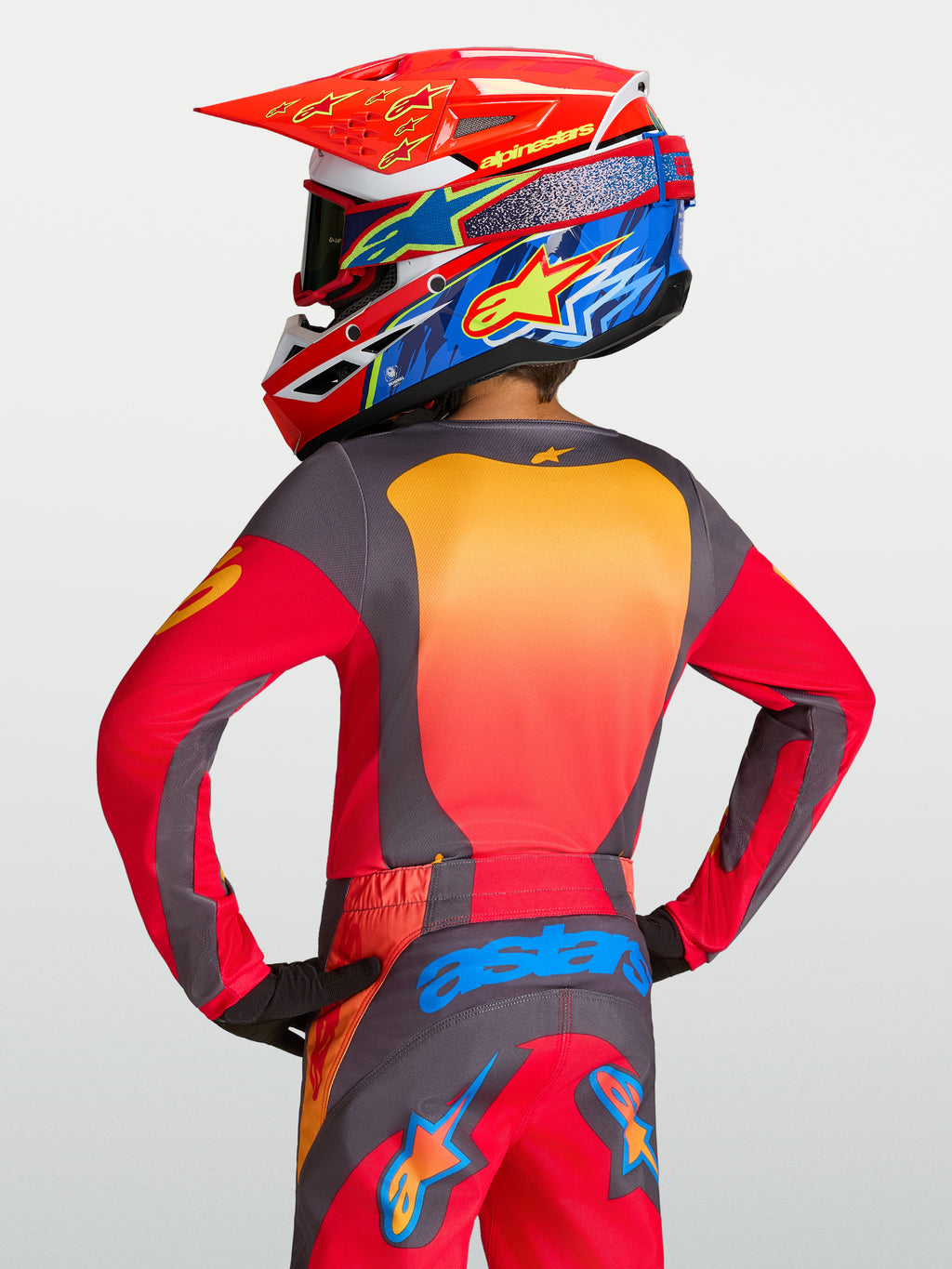 Alpinestars Maglia Fluid Hunt Ragazzo 2027, maglia MX rossa e grigia, vista posteriore su pilota, vestibilità atletica.