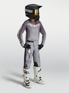 Alpinestars Ragazzo Fluid Amber Gear Set, completo da motocross grigio, maglia e pantaloni, stivali bianchi e casco nero.