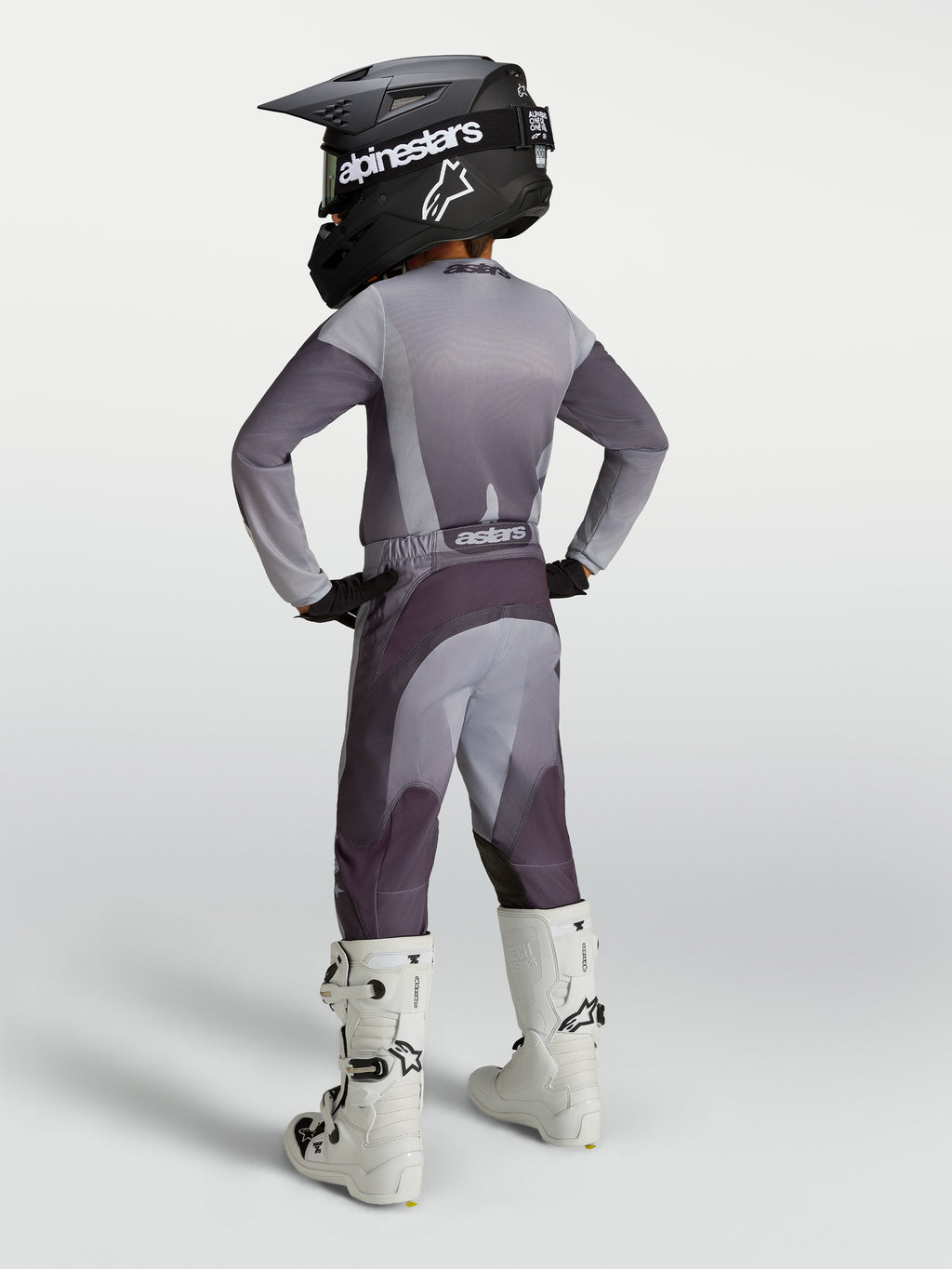 Alpinestars Ragazzo Fluid Amber Gear Set 2027, completo da motocross grigio e viola con casco e stivali bianchi, vista posteriore.