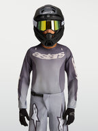 Alpinestars Maglia Fluid Amber Ragazzo 2027, maglia da motocross grigio e ambra, traspirante per fuoristrada, indossata da un pilota.