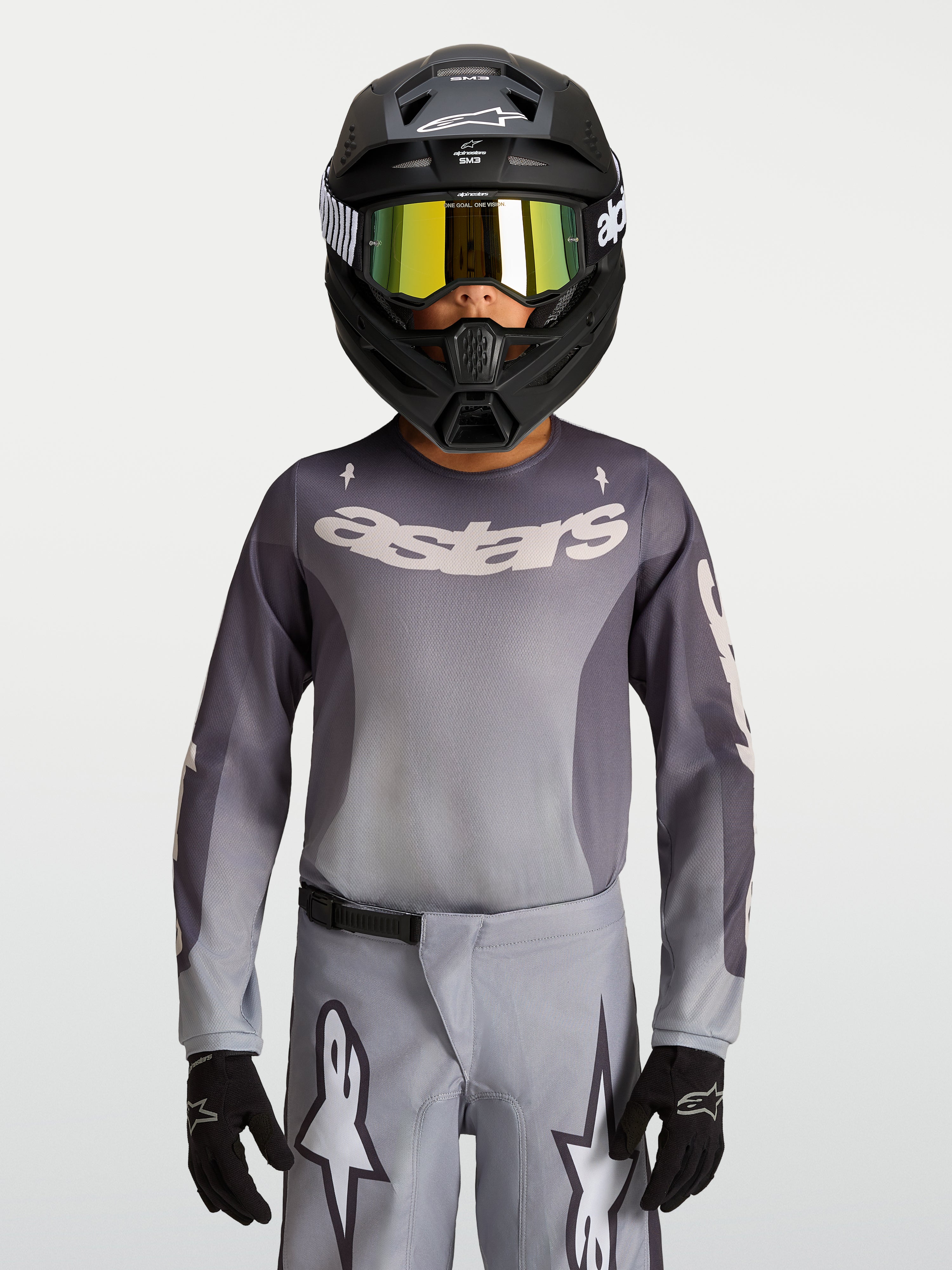 Alpinestars Maglia Fluid Amber Ragazzo 2027, maglia da motocross grigio e ambra, traspirante per fuoristrada, indossata da un pilota.